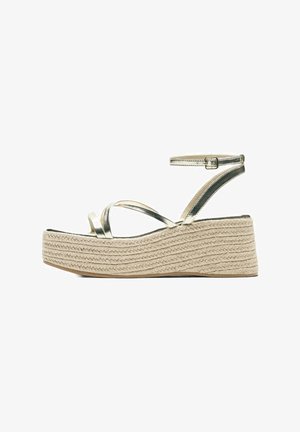 Kile-espadrillesandal med metalliske gyldne remme, ankelspænde og flettet juteplatformsål, set fra siden på hvid baggrund.