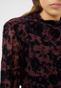 Durchsichtige Bluse mit langen Ärmeln, gefertigt aus einem strukturierten, dunkelburgunderfarbenen Stoff mit einem schwarzen Blumenmuster, rundem Ausschnitt und weichem Fall.