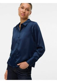 Mörkblå satinskjorta med lång ärm, knappfront och krage. Slät textur och skräddarsydd passform. Minimal detaljering, kombinerad med mörka jeans.