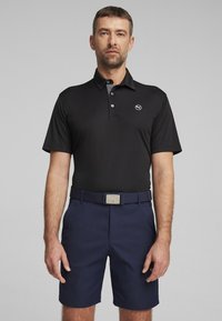Čierne polo tričko s krátkymi rukávmi, s šedým golierom a logom. V kombinácii s námorníckymi šortkami a zodpovedajúcim opaskom so striebornou prackou.