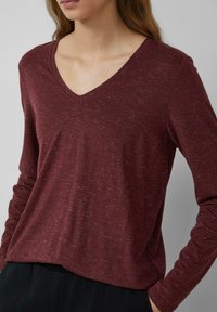 Bordeaux lange mouw top met een v-halsontwerp, gemaakt van een textuur gebreide stof met subtiele lichte spikkels. Ontspannen pasvorm, minimale details.