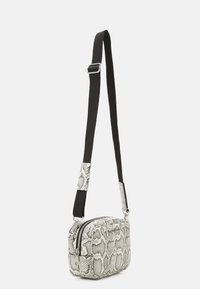 Liten axelremsväska i svart och vit ormskinnsmönster. Texturerat syntetiskt material, silverfärgad hårdvara, justerbar rem, dubbel dragkedjestängning.