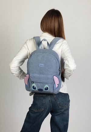 Blauwe corduroy rugzak met een cartoon Stitch gezicht, met roze oren en grote ogen. Heeft verstelbare schouderbanden en een voorkant met een ritszak.