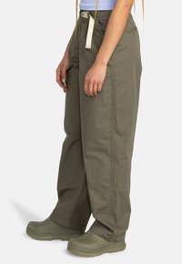 Olive green cargo pants with a loose fit, drawstring waist, and side pockets, made of lightweight fabric. Worn with green shoes.