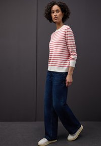 Stribet sweater i hvid og pink, lagdelt over blå jeans med vide ben. Har ribbede manchetter og kant, kombineret med hvide sneakers.