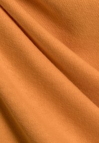 Textielstof in zacht oranje katoen met een gladde textuur, voorzien van een subtiel gebreid patroon en gedrapeerde plooien.