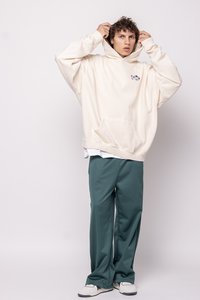 Sudadera crema holgada con un bolsillo frontal y logotipo, combinada con pantalones verdes sueltos. La textura es notablemente suave, adecuada para un uso casual.