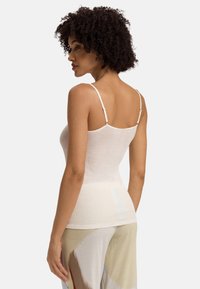 Top a canotta bianca a coste con spalline sottili e regolabili, caratterizzato da un design aderente e una texture liscia, abbinato a pantaloni larghi con fantasia.