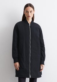 Veste bomber noire avec fermeture éclair à l'avant, poignets côtelés, poches latérales et texture lisse. Présente un design minimaliste et une coupe ajustée.