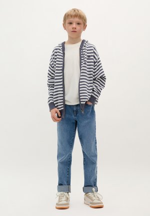 Felpa a righe blu navy e bianca, tessuto leggero, bordi grigi, indossata sopra una t-shirt bianca. Jeans in denim azzurro, con fondo arrotolato, sneakers neutre.