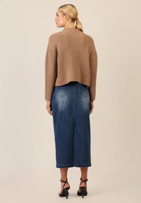 Brauner gerippter Pullover mit einem verkürzten Rücken, kombiniert mit einem blauen Denim-Rock mit gepunkteten Akzenten und einem langen, geraden Schnitt. Schwarze Riemchensandalen.