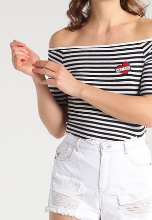 Schwarz-weißer gestreifter Off-Shoulder-Top mit Herzstickerei, kombiniert mit weißen, lässigen Shorts mit ausgefransten Kanten und Taschen.