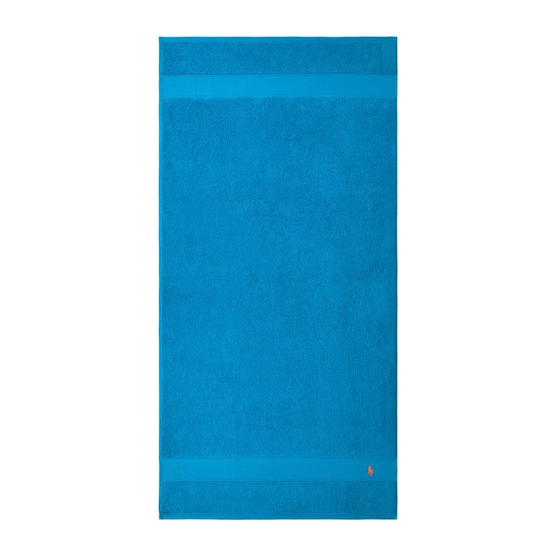 Πετσέτα μπάνιου τιρκουάζ με υφασμάτινη επιφάνεια, που διαθέτει μια λεία ταινία στο πάνω μέρος και ένα μικρό διακοσμητικό λογότυπο στο κάτω δεξί μέρος.