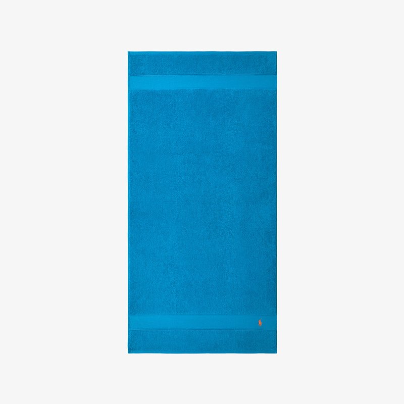 Πετσέτα μπάνιου τιρκουάζ με υφασμάτινη επιφάνεια, που διαθέτει μια λεία ταινία στο πάνω μέρος και ένα μικρό διακοσμητικό λογότυπο στο κάτω δεξί μέρος.