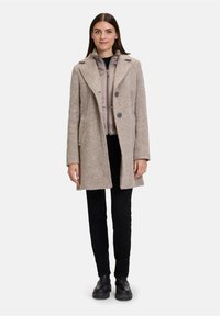 Beige wollen blend jas met een getailleerde pasvorm, notch-kraag, dubbele knopen en zijzakken, gedragen over een lichte zip-up jacket.