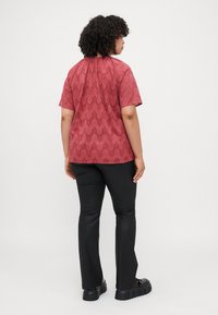 Top corto a maniche corte rosso con un design a motivi, abbinato a pantaloni neri aderenti e scarpe nere chunky.