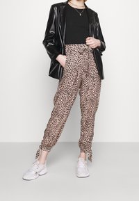 Černý lesklý blazer, černý top a béžové kalhoty s leopardím potiskem, které mají stahovací šňůrku a vázání na kotnících; v kombinaci s bílými teniskami.