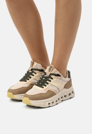 Baskets chunky avec tige synthétique beige, lacets verts olive, accents en daim et épaisse semelle en caoutchouc blanc avec découpes.