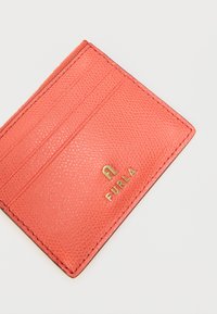 Δερμάτινη θήκη καρτών σε κοραλλί χρώμα με υφή, χρυσό λογότυπο 'FURLA', τρεις θήκες για κάρτες και ραμμένα άκρα. Συμπαγής ορθογώνιος σχεδιασμός.