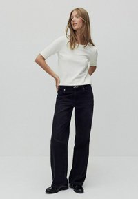 Hvid kortærmet top parret med højtaljede, brede sorte jeans; struktureret stof med en glat overflade; sorte sko fuldender outfittet.