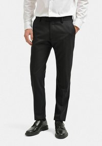 Svarta skräddarsydda byxor i slätt tyg, med rak skärning, bälteöglor och sidofickor, matchade med svarta klackskor.