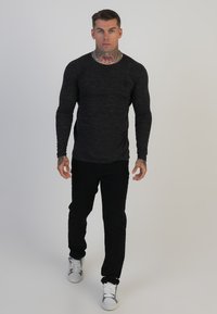 Fekete, hosszú ujjú póló, texturált felülettel, fekete, testhez simuló nadrággal és fehér sportcipővel párosítva, egy személynél bemutatva.