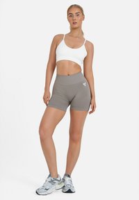 Športni modrček v beli barvi in visoko pasne kratke hlače v svetlo sivi barvi. Tkanina je gladka in oprijeta, s podrobnostjo logotipa na hlačah.