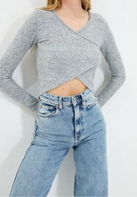 Grå langærmet top med indpakningsdesign, parret med højtaljede lyseblå denim jeans med lommer og en falmet tekstur.
