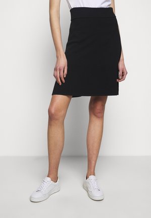 Falda negra hasta la rodilla con cintura ajustada, tela texturizada y abertura lateral, combinada con zapatillas blancas. Diseño simple y minimalista.