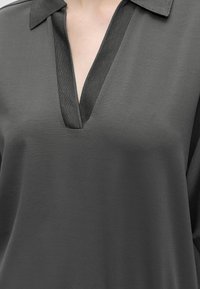 Chemise gris foncé avec un col en V profond et un col plat, montrant une partie de la poitrine et du cou supérieurs d'une personne.