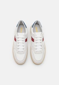 Sneaker in pelle bianca con accenti rossi e blu, punta rotonda, lacci e suola in gomma beige. Pannelli testurizzati notevoli sui lati.