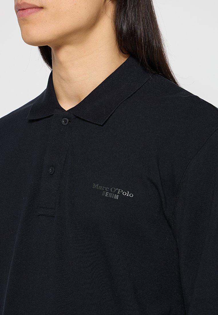 Schwarzes Poloshirt aus strukturiertem Stoff, mit einem Kragen, einer zwei-knopfigen Leiste und einem dezenten Logo, das auf der Brust gestickt ist.
