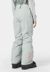 Světle modré sněhové kalhoty vyrobené z vodoodpudivého materiálu, s volným střihem, elastickým pasem a oranžovým logem "HELLY HANSEN" na boku.