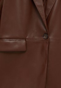 Gros plan d'un blazer en cuir marron avec un seul bouton foncé et une poche à rabat à l'avant.