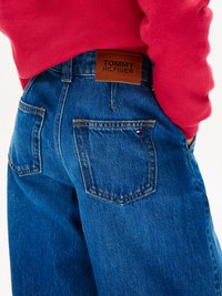 Tamsiai mėlyni džinsai su laisvu siluetu, turintys dvi užpakalines kišenes ir rudą odinį ženklą su įspaustu užrašu "TOMMY HILFIGER".