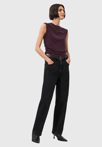 Top violet tanpa lengan dengan sisi berkerut dipadukan dengan celana jeans hitam berpinggang tinggi dan sepatu hak runcing hitam; kain bertekstur dan permukaan halus.