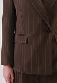 Blazer marrone a righe sottili in un design strutturato, caratterizzato da un singolo bottone nero, rever con tacca e tasche laterali.