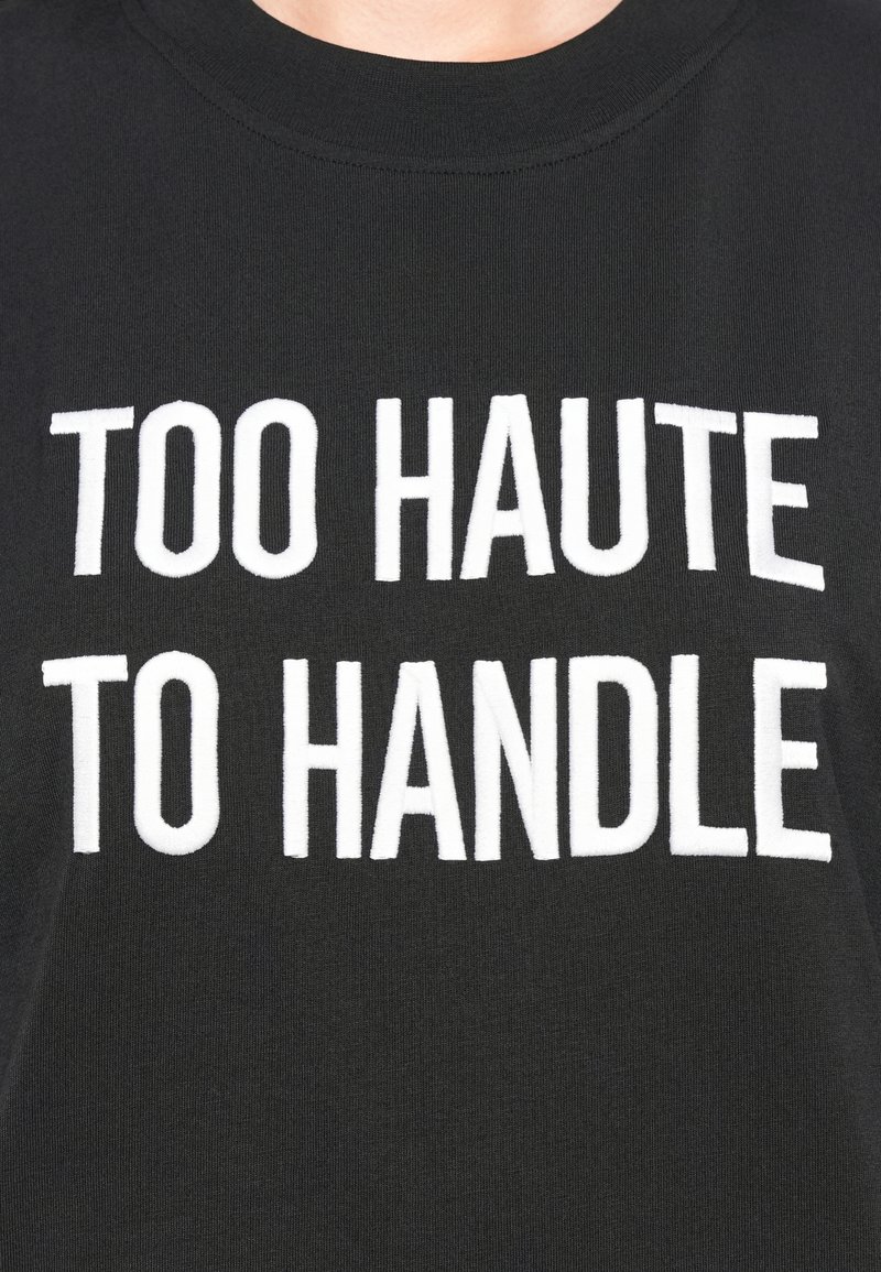 Schwarzes Baumwoll-T-Shirt mit kräftigem weißen Text, der "TOO HAUTE TO HANDLE" in einem entspannten Schnitt zeigt.