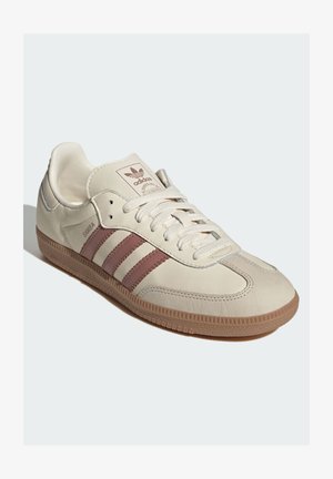 Beige læder-sneaker med brune accenter, der har tre signaturstriber, rundet tå og tekstureret gummi-sål i hampfarve.