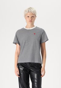 T-shirt à rayures noir et blanc, en coton, avec un col rond côtelé, des manches courtes, arborant un petit emblème en forme de cœur rouge sur la poitrine.