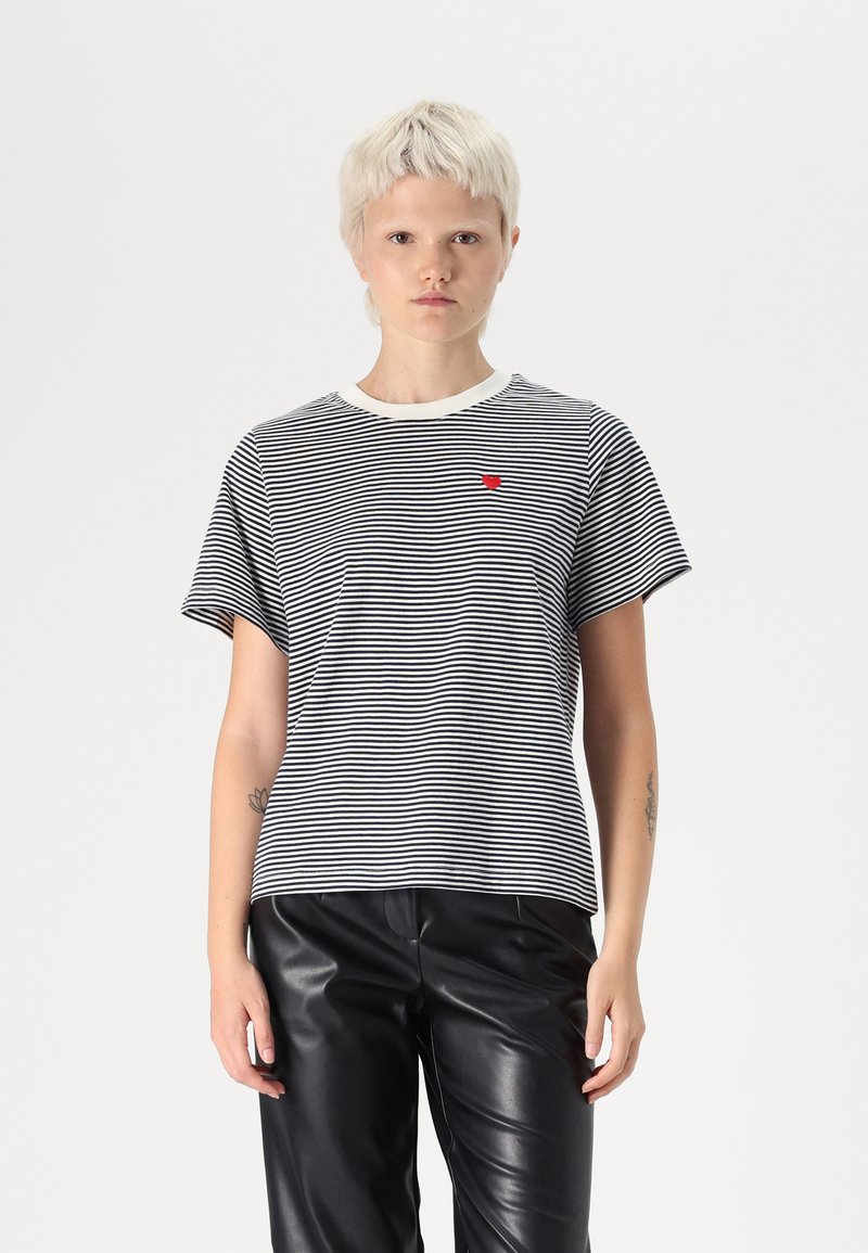 T-shirt à rayures noir et blanc, en coton, avec un col rond côtelé, des manches courtes, arborant un petit emblème en forme de cœur rouge sur la poitrine.
