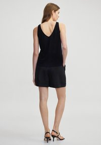 Zwarte mouwloze top met een V-vormige rugontwerp, gecombineerd met bijpassende zwarte shorts. Glad textuur en eenvoudige snit, met zijkanten pockets.