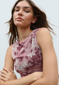 Haut sans manches, de style portefeuille, en tissu léger et doux, présentant un motif tie-dye floral rose et mauve avec une texture lisse.