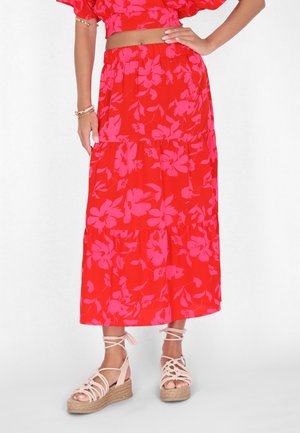 Jupe maxi rouge avec des motifs floraux roses, design à volants et taille élastique. Associée à des sandales compensées à lanières.