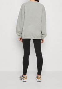 Sudadera gris de gran tamaño con hombros caídos, combinada con mallas negras ajustadas. La modelo lleva zapatos deportivos multicolores.
