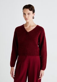 Burgundy cropped cardigan with a V-neck, long sleeves, and button closure. Soft texture with ribbed hem and solid color finish.