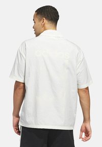 Camicia a maniche corte in bianco sporco, tessuto testurizzato, con colletto a bottoni e stampa logo discreta sul retro. Vestibilità rilassata e orlo dritto.