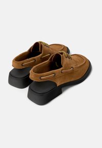 Zapatos de ante marrón, tipo slip-on, con una suela plataforma negra baja, que presentan detalles en verde y cordones a los lados.