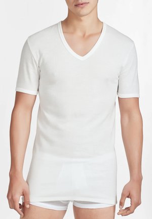 T-shirt bianco a maniche corte con scollatura a V e bordi a contrasto. Materiale morbido e leggero, design aderente e texture liscia. Indossato sopra slip bianchi.