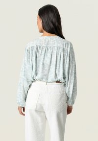 Blusa azzurro chiaro con un motivo testurizzato e vestibilità rilassata, abbinata a pantaloni bianchi a vita alta con due tasche posteriori.